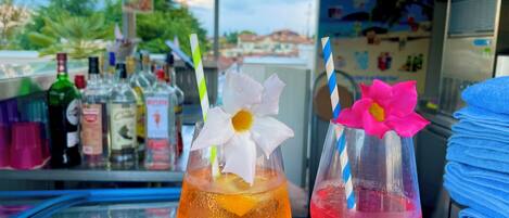 Dos cócteles con adornos florales sobre una barra, rodeados de diversas botellas y un tablero de menú.