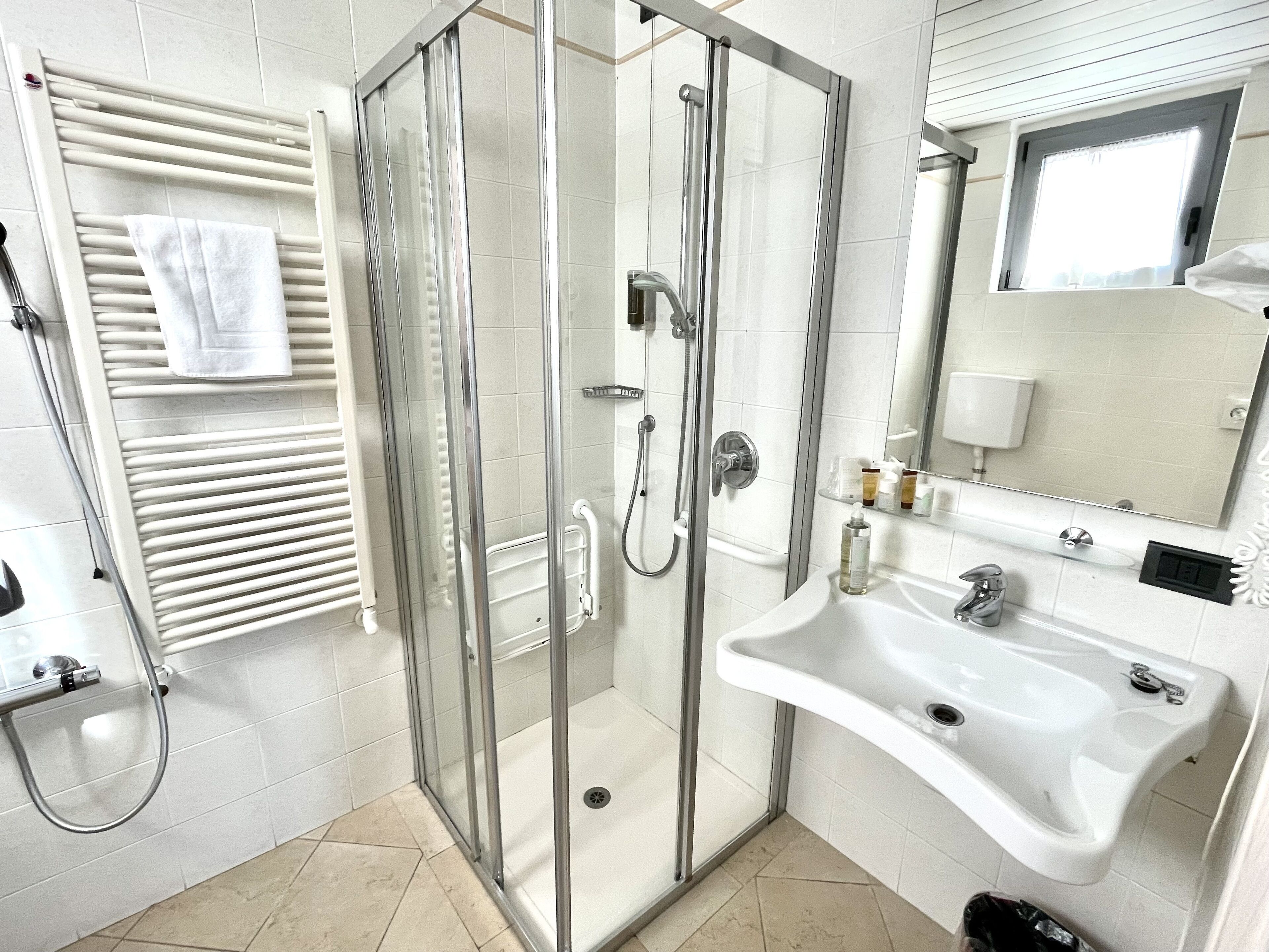 A modern bathroom with a glass-enclosed shower, a white sink, and a towel rack.