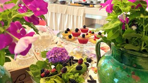 A table with various food items and flowers, including a glass pitcher and a vase with flowers. - Hotel Alfieri (Sirmione)