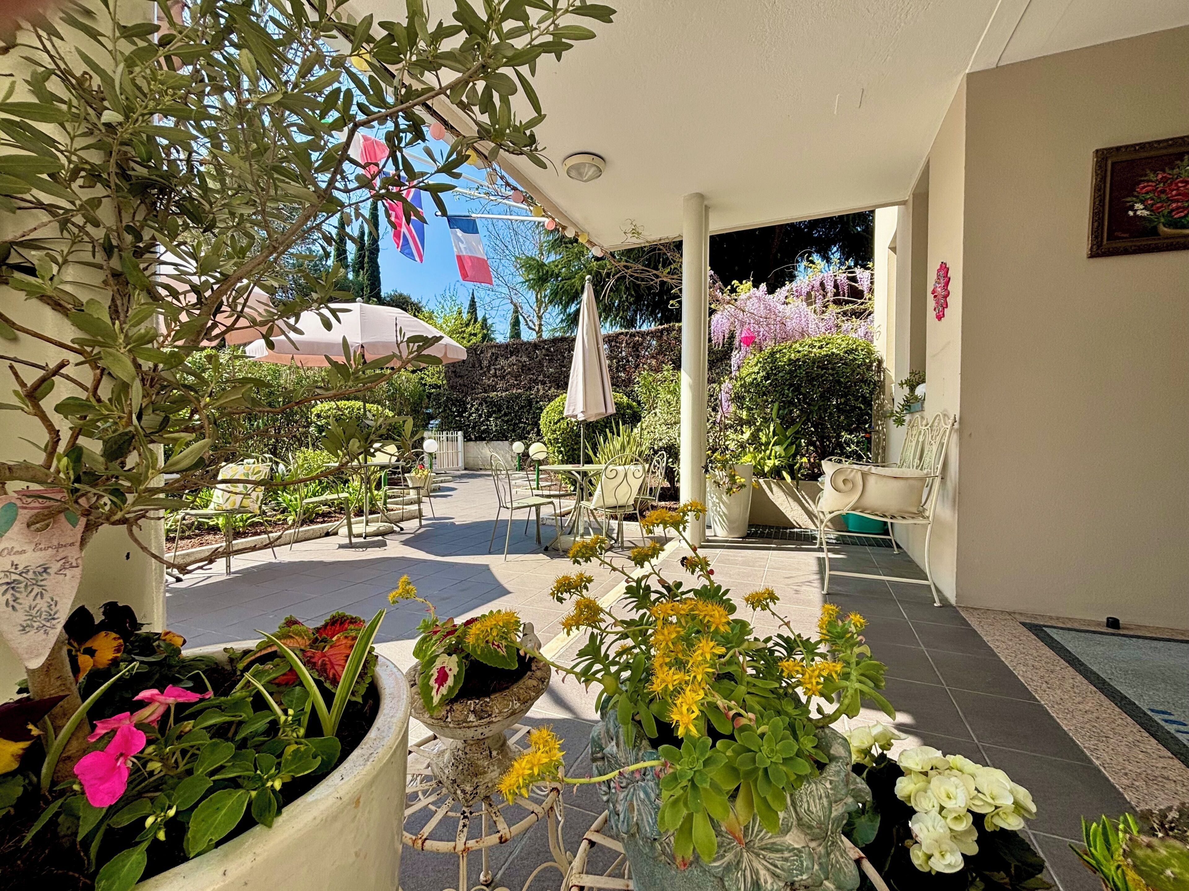 Eine Außenpatio-Terrasse mit Tischen, Stühlen, Blumentöpfen und Blick zum Himmel.