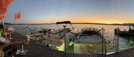 A wooden deck with boats docked, a table with chairs, and a view of the water at sunset.
