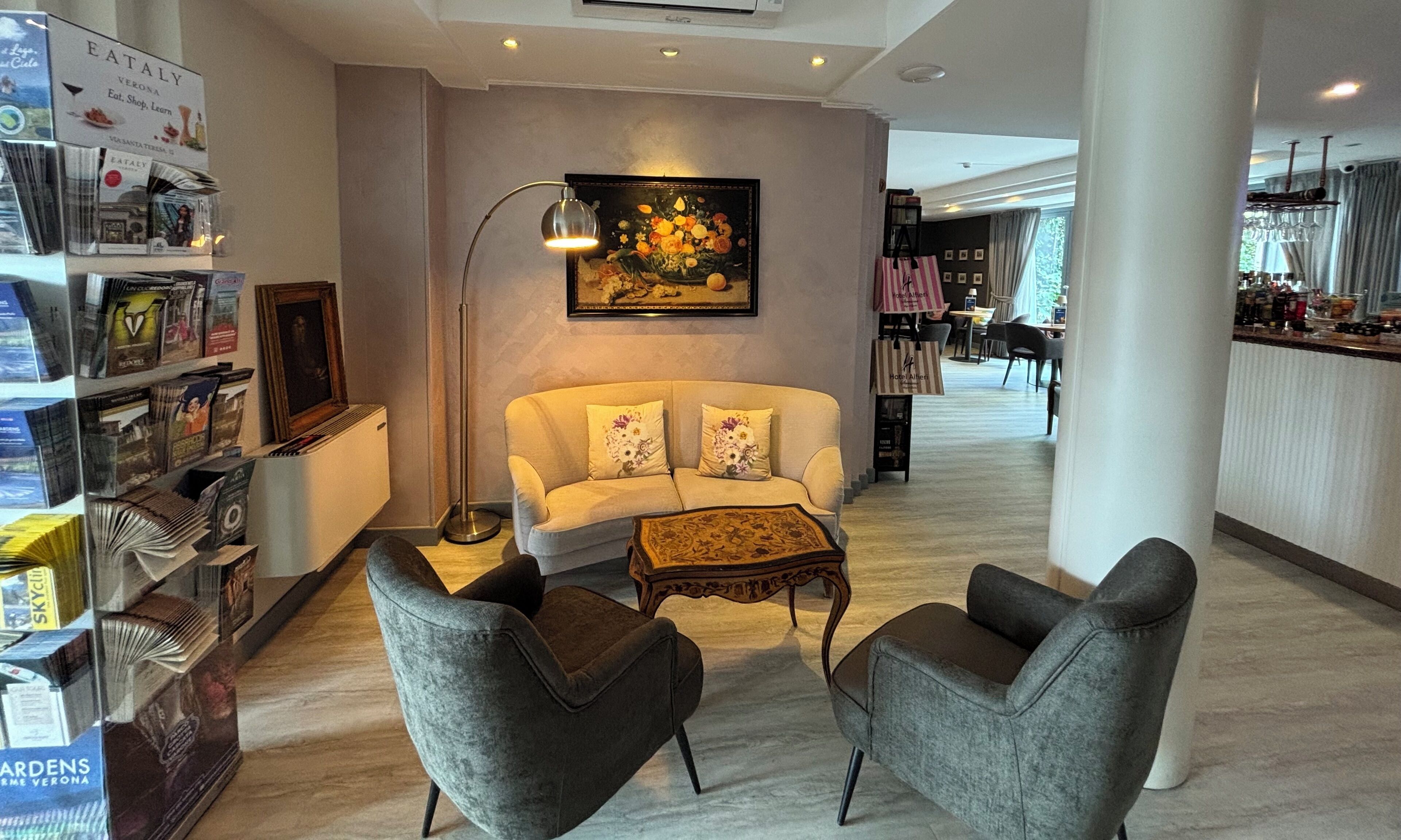 Un hall d’hôtel moderne avec un canapé, deux fauteuils, une lampe sur pied et un tableau.
