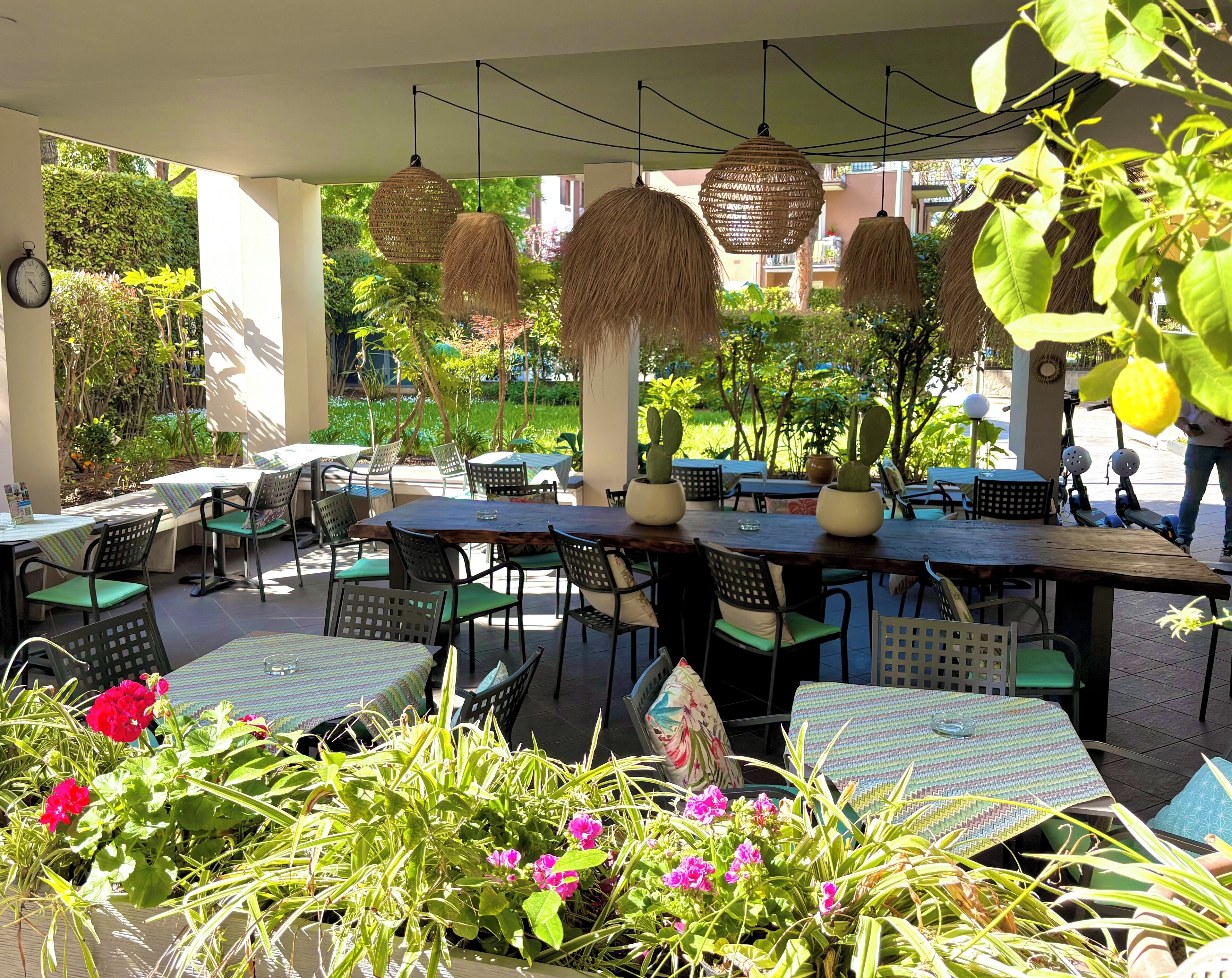 Un espace extérieur aménagé avec des tables et des chaises, entouré de verdure et de plantes en pot.