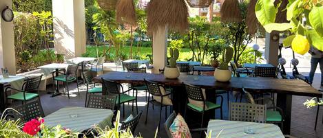 Un espace extérieur aménagé avec des tables et des chaises, entouré de verdure et de plantes en pot.