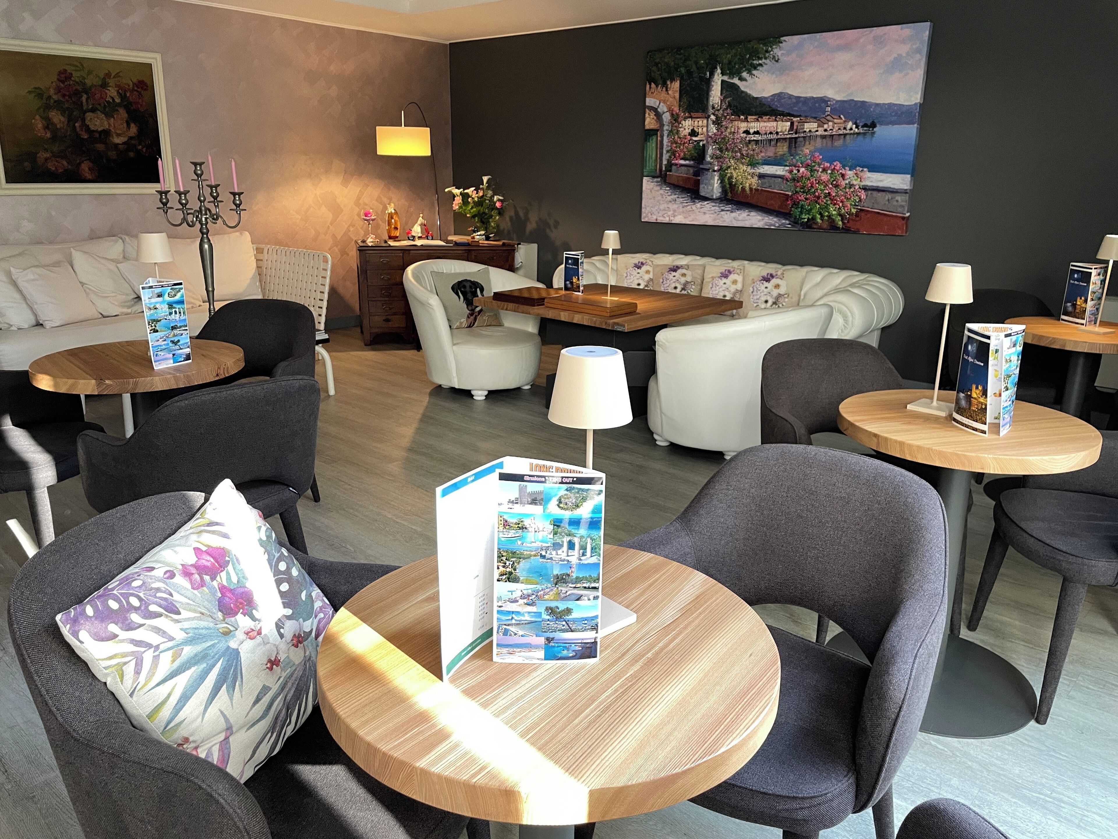 A modern lounge area with sofas, armchairs, and round tables, featuring a large painting and a candelabra.