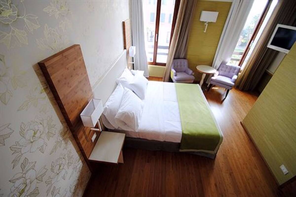 Een hotelkamer met een houten bed, een klein rond tafeltje, een stoel en een televisie aan de muur.