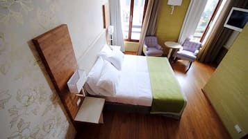A hotel room with a wooden bed, a small round table, a chair, and a TV on the wall.