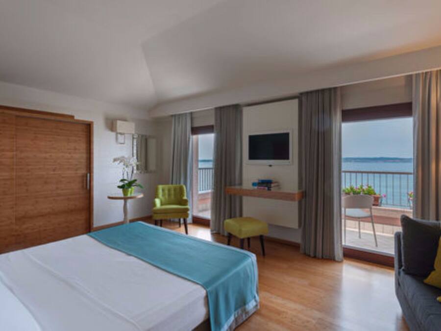 Ein Hotelzimmer mit Bett, Schreibtisch, Fernseher, einem Balkon mit Meerblick und einer Sitzecke mit Sofa und Sesseln.