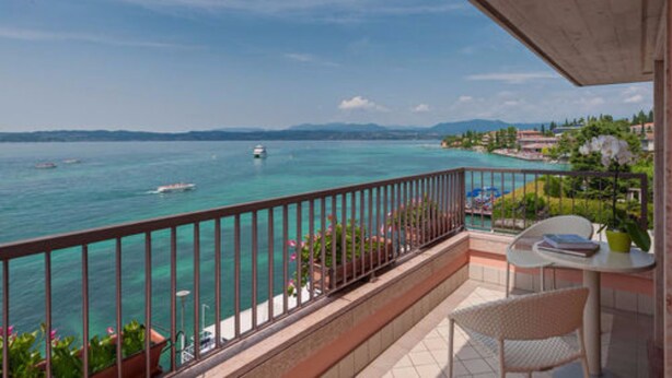 A balcony with a view of the sea, a table with chairs, and potted plants. - Hotel Eden (Sirmione)