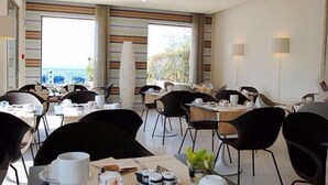 A modern dining area with tables and chairs, a view of the sea, and a large window with curtains. - Hotel Eden (Sirmione)