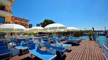 Terraza con sillones azules y sombrillas blancas, con vista a un cuerpo de agua.