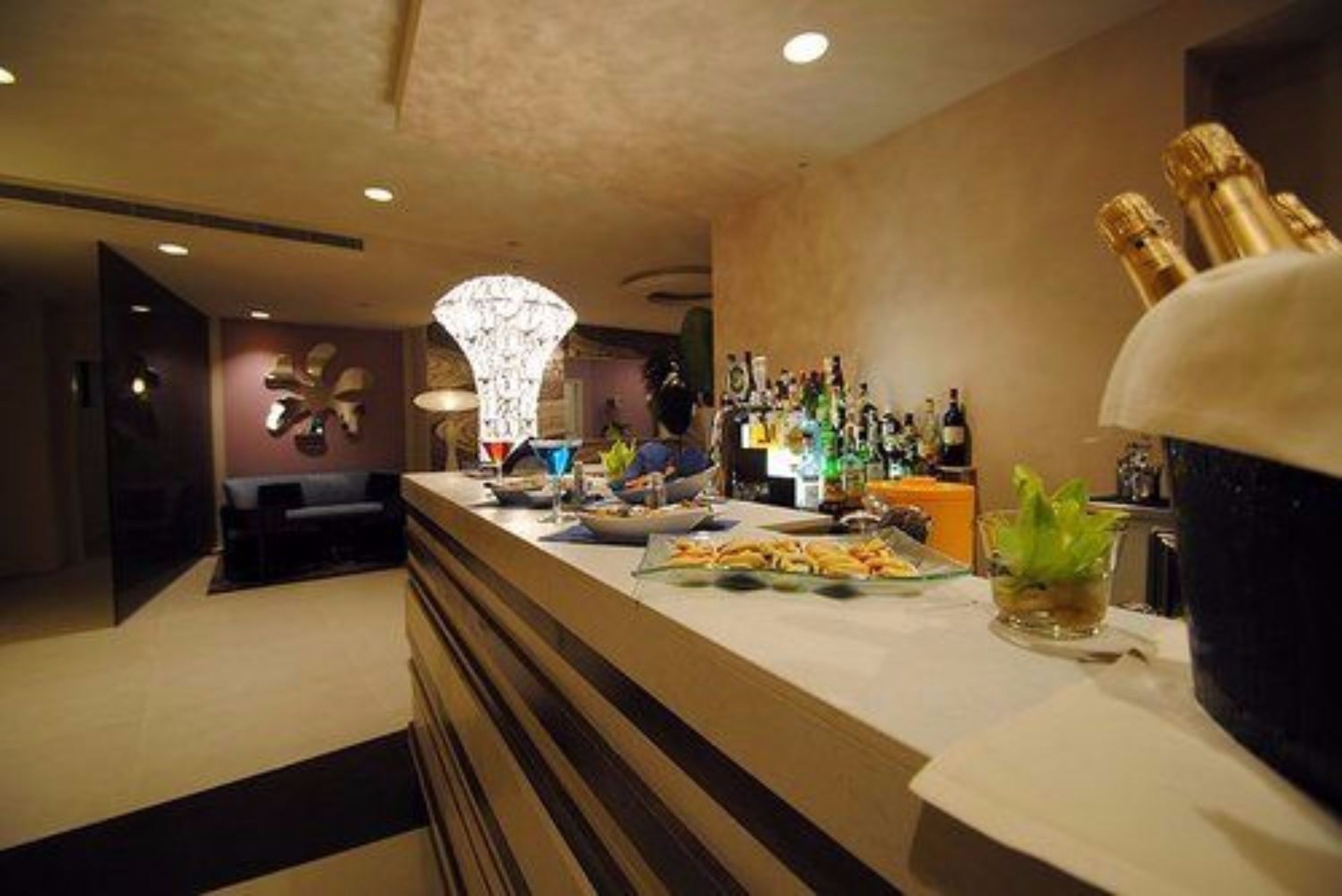 A bar area with a counter, bottles, and glasses. There is a decorative light fixture above the counter.