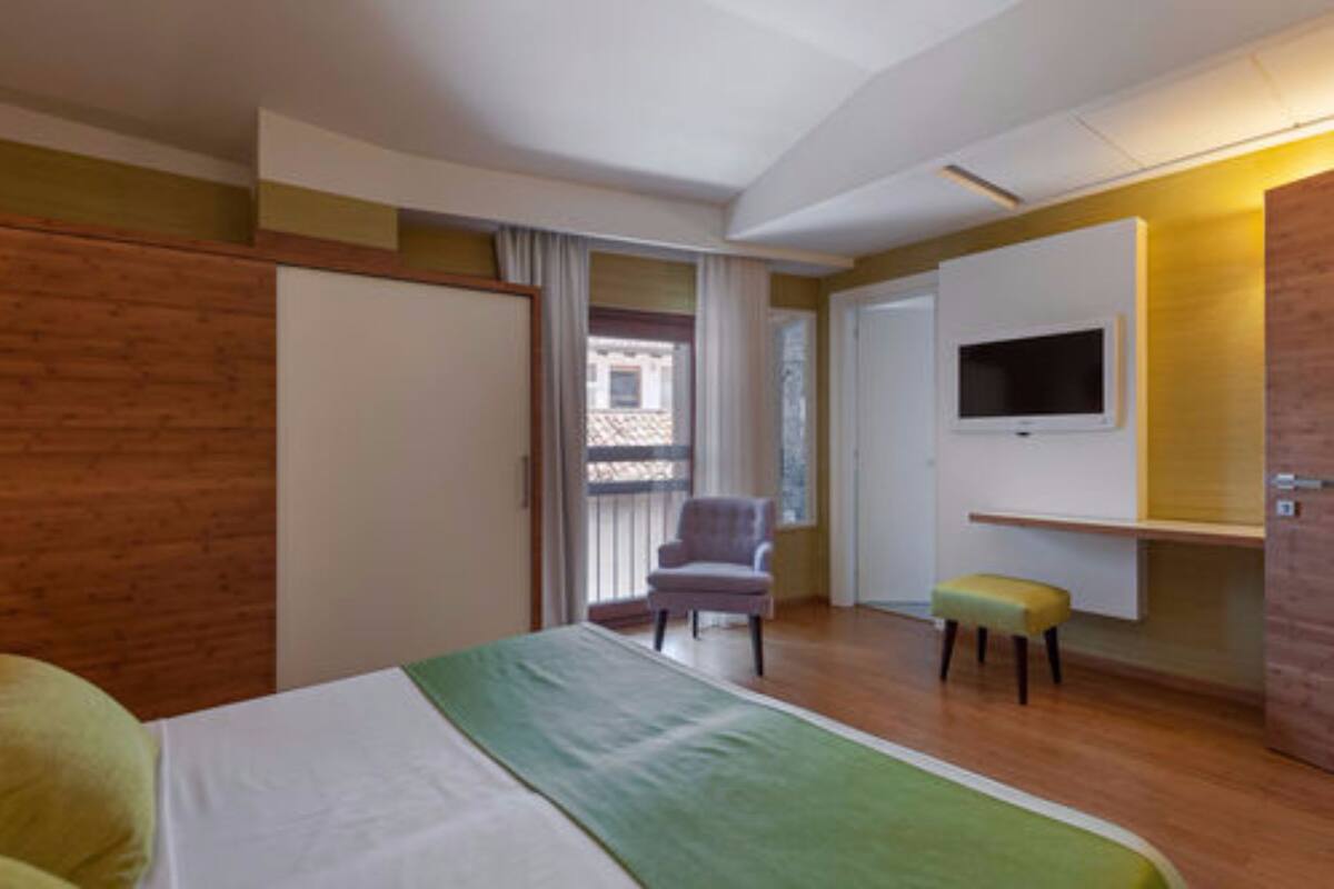 Een hotelkamer met een bed, een stoel, een aan de muur bevestigde televisie en een klein tafeltje.