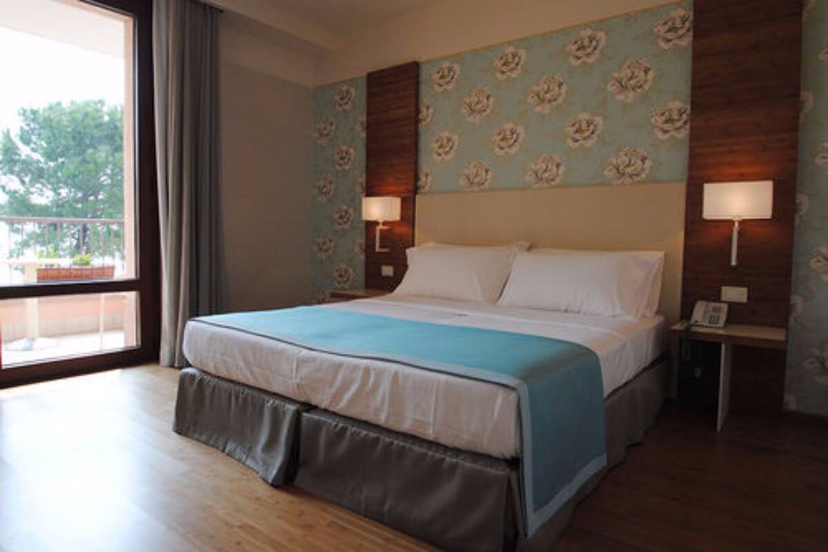 Een hotelkamer met een groot bed, een raam met gordijnen, een houten vloer en een wand met bloemenbehang.