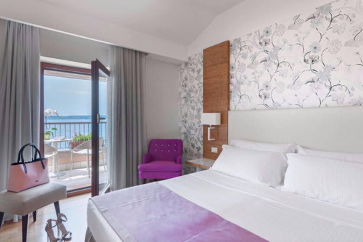 Een hotelkamer met een bed, een stoel, een tafel en uitzicht op zee vanaf een balkon.