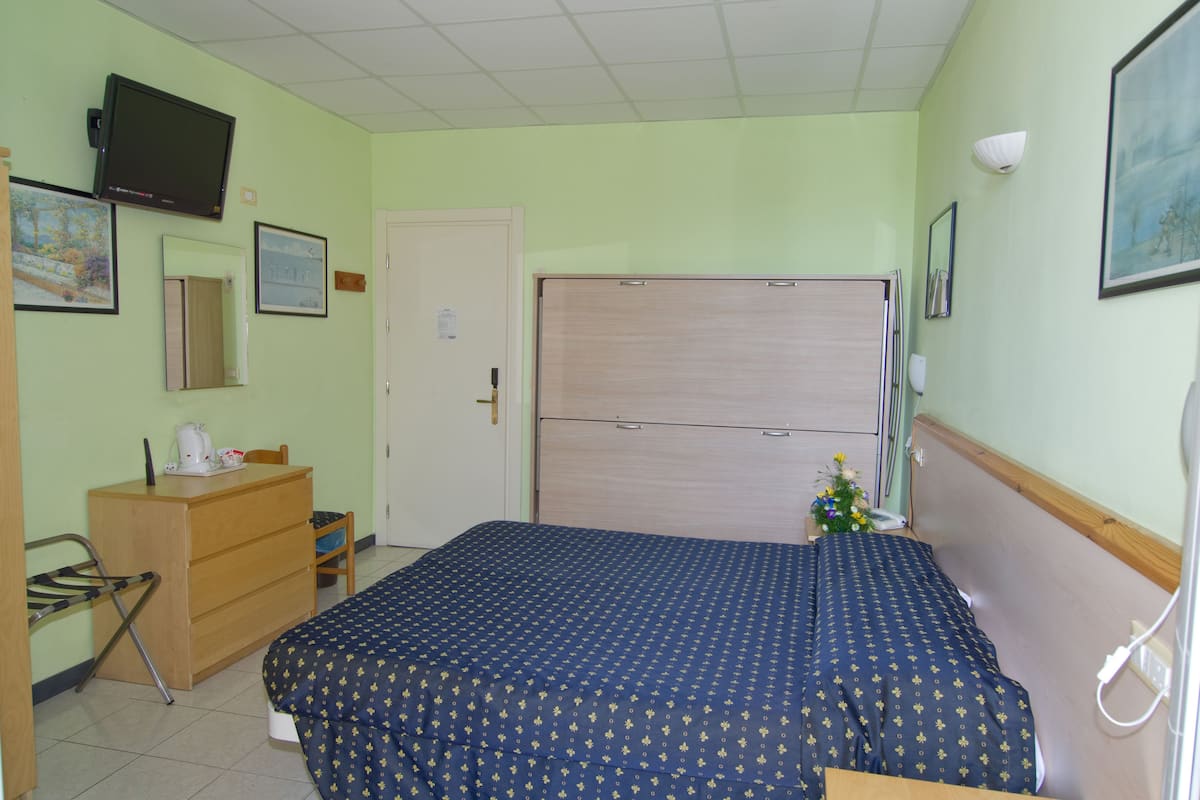 A bedroom with a bed, dresser, and a television mounted on the wall.