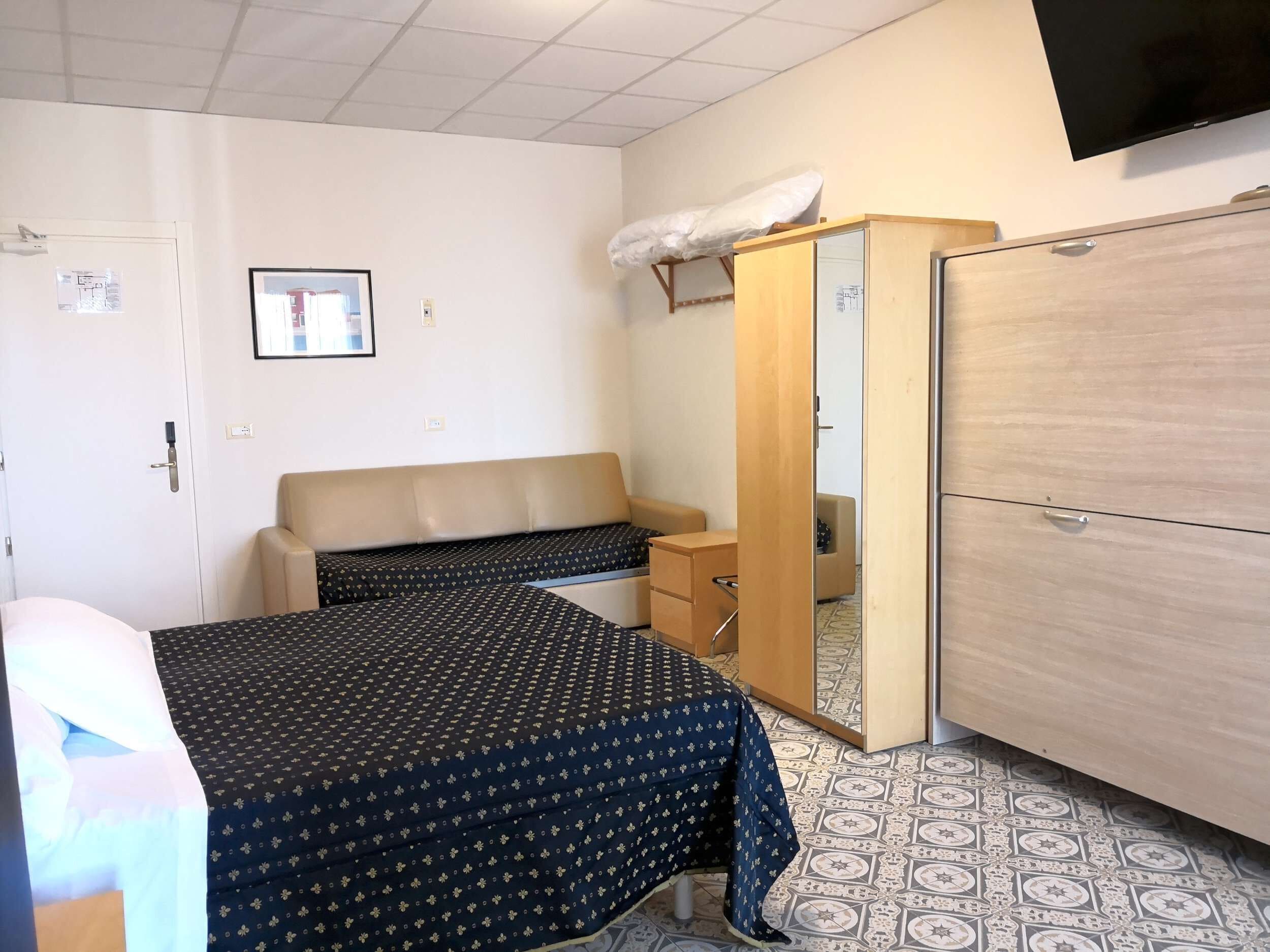 Hotellihuone, jossa on sänky, sohva, vaatekaappi, työpöytä ja televisio.