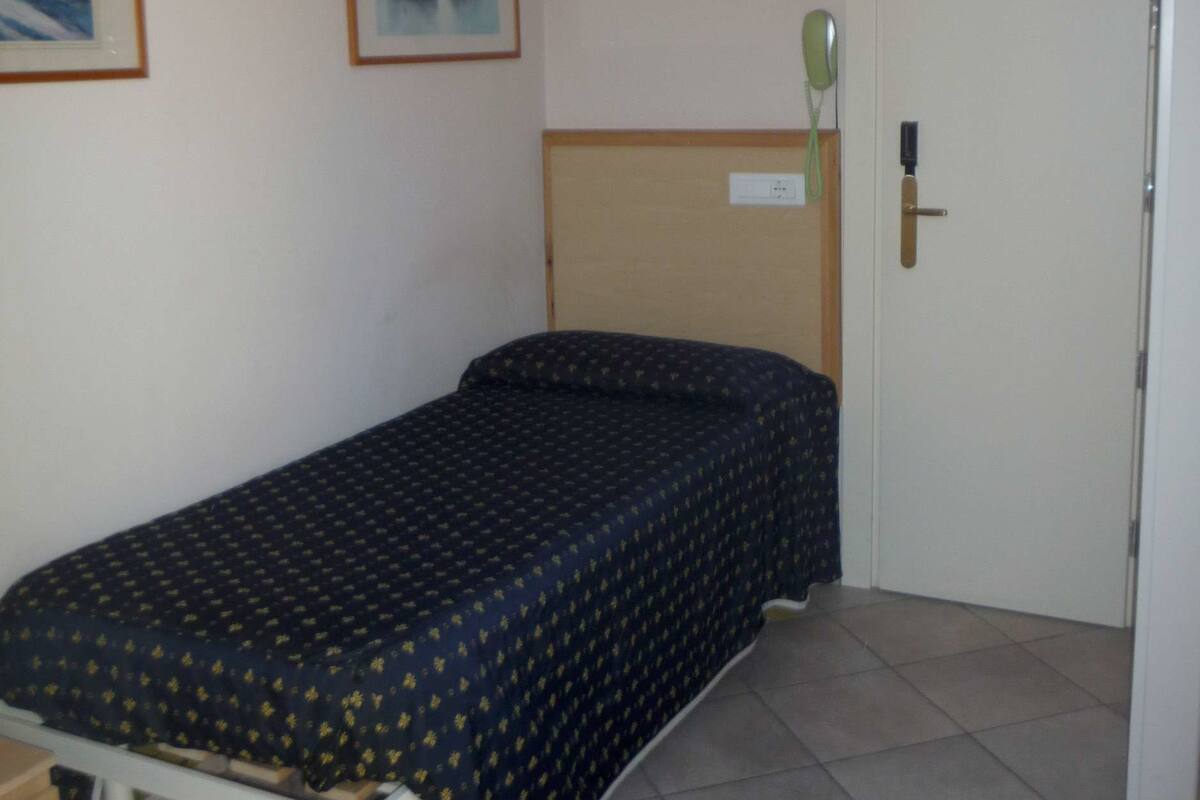A small, single-bed room with a wooden headboard, a bedside table, and a door with a keyhole.