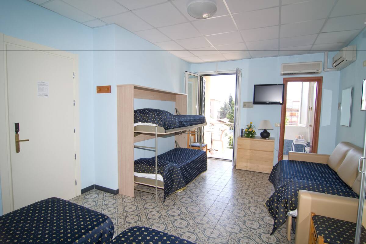 A dormitory room with bunk beds, a desk, a chair, and a television.