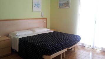 Un dormitorio con cama, mesita de noche, lámpara de pared y dos cuadros enmarcados.