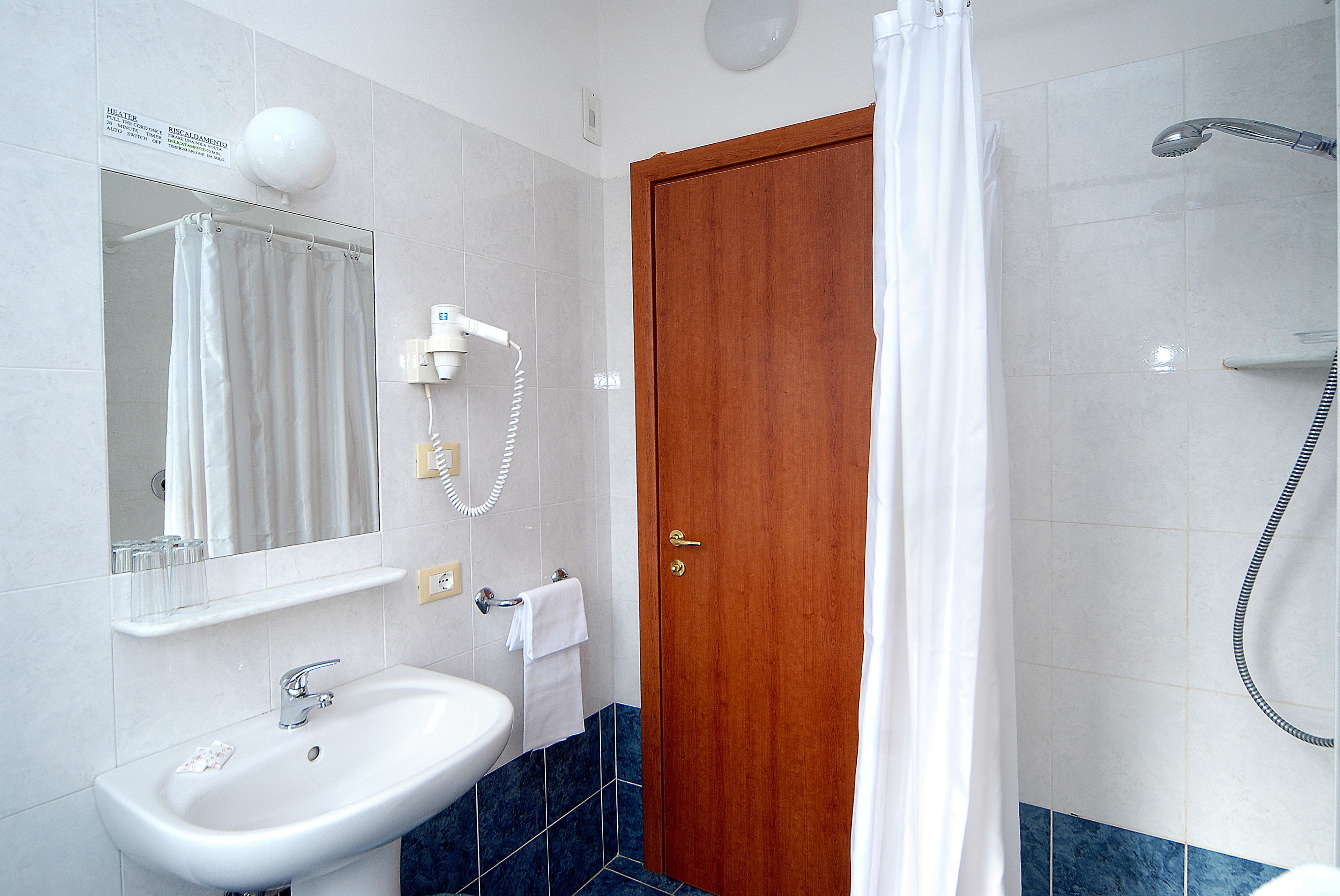 A bathroom with a white sink, a mirror, a shower, and a wooden door.