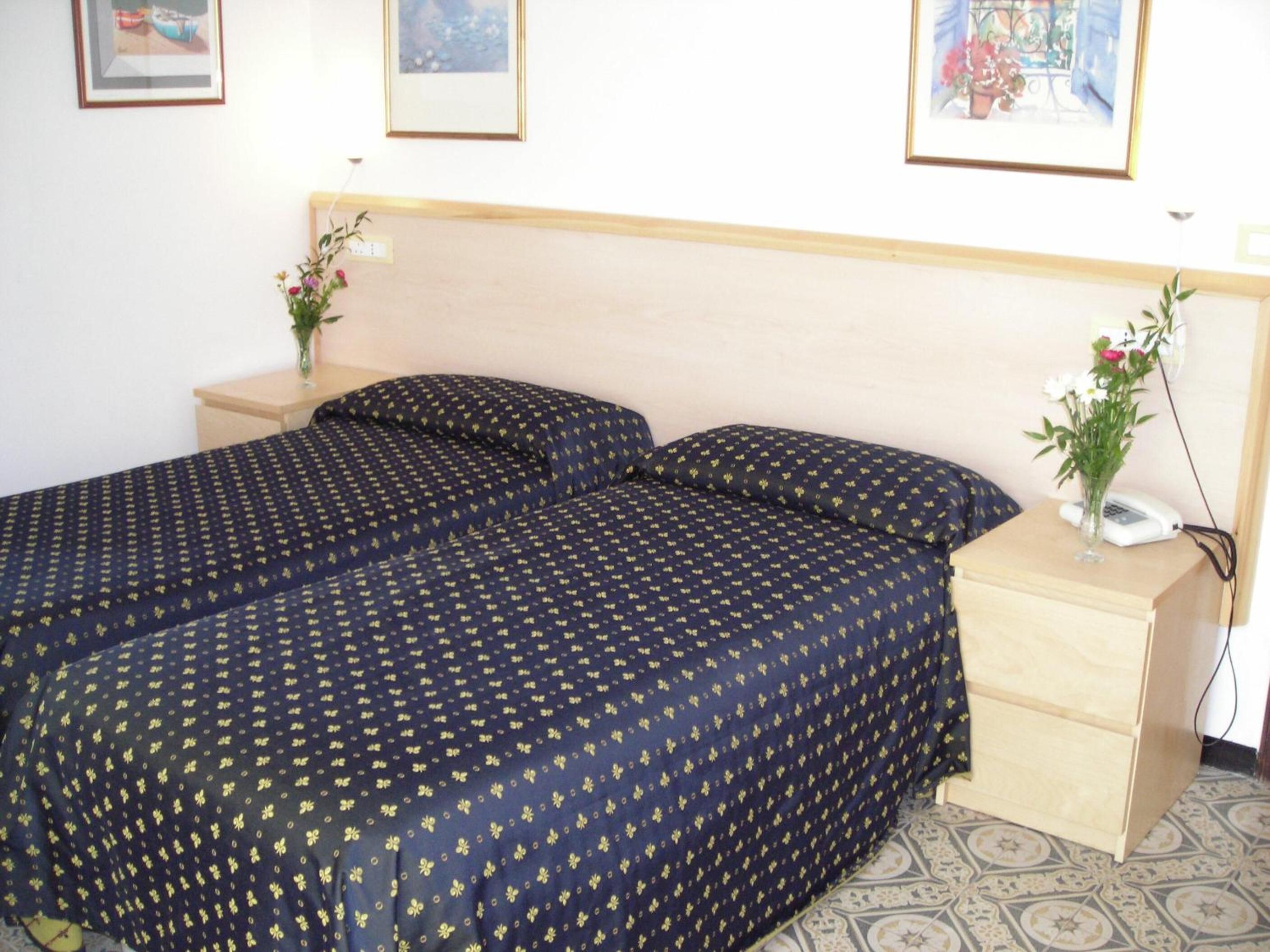 Un dormitorio con una cama, dos mesitas de noche y una mesilla con un jarrón de flores.