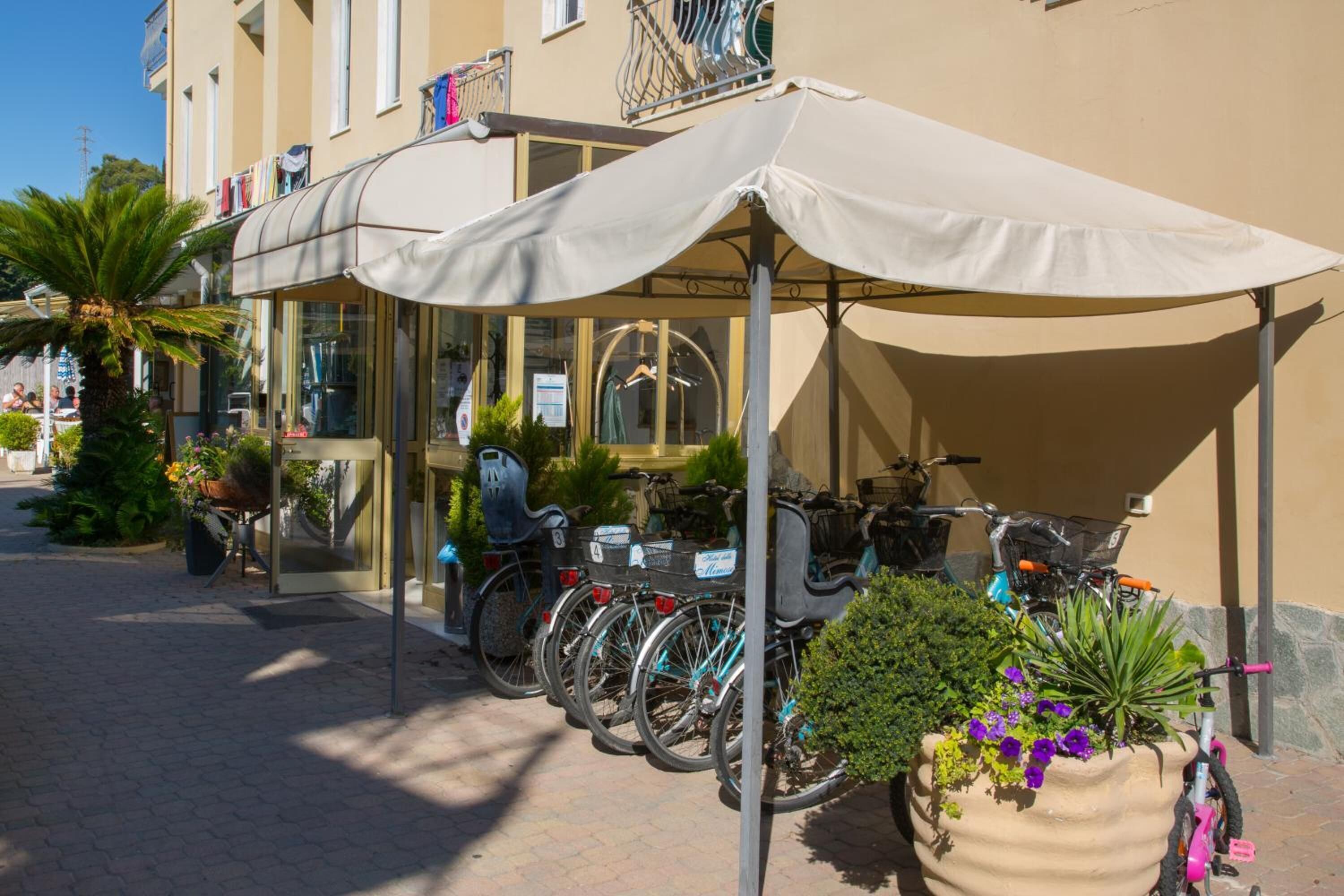 Várias bicicletas estacionadas sob uma cobertura, com um vaso grande próximo.
