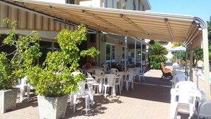 An outdoor seating area with white plastic chairs and tables, potted plants, and a covered patio.