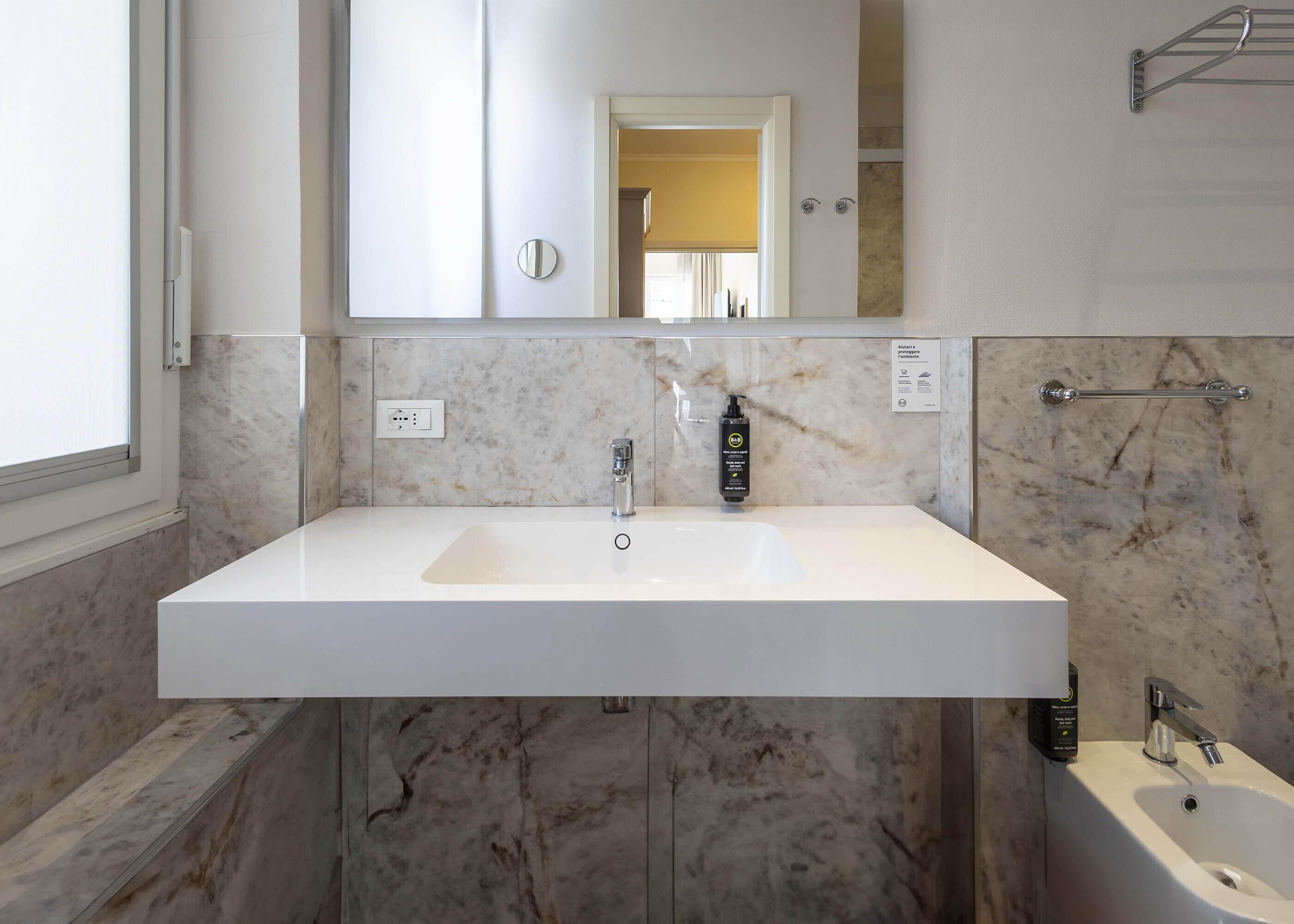 A bathroom with a white sink, a mirror, and a marble wall.