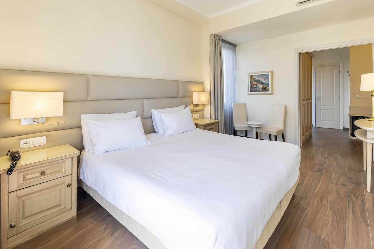 Ein Hotelzimmer mit einem großen Bett, Nachttischen mit Lampen, einem Sessel und einem Schreibtisch.