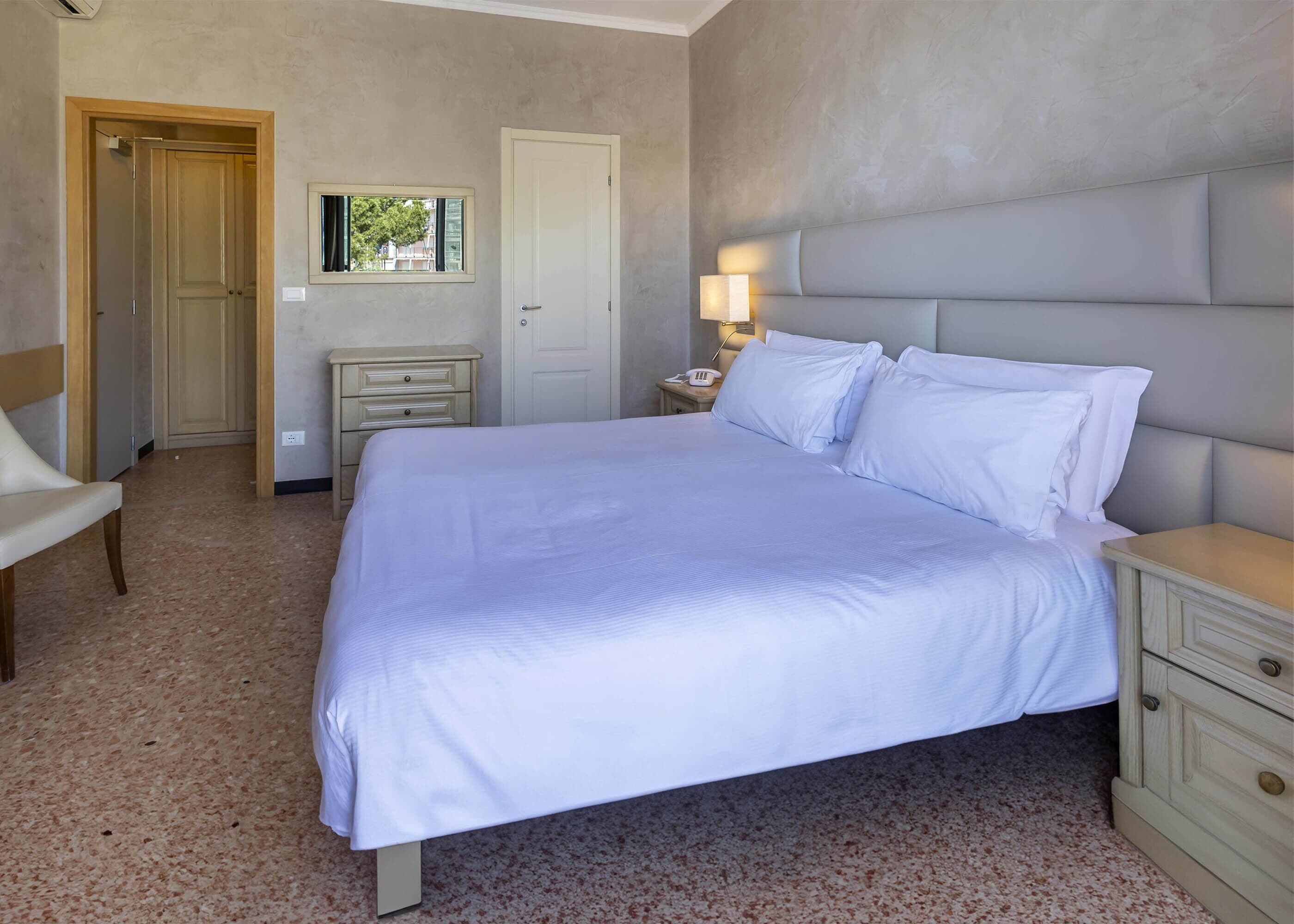 A bedroom with a large bed, a bedside table with a lamp, a chair, and a wardrobe.