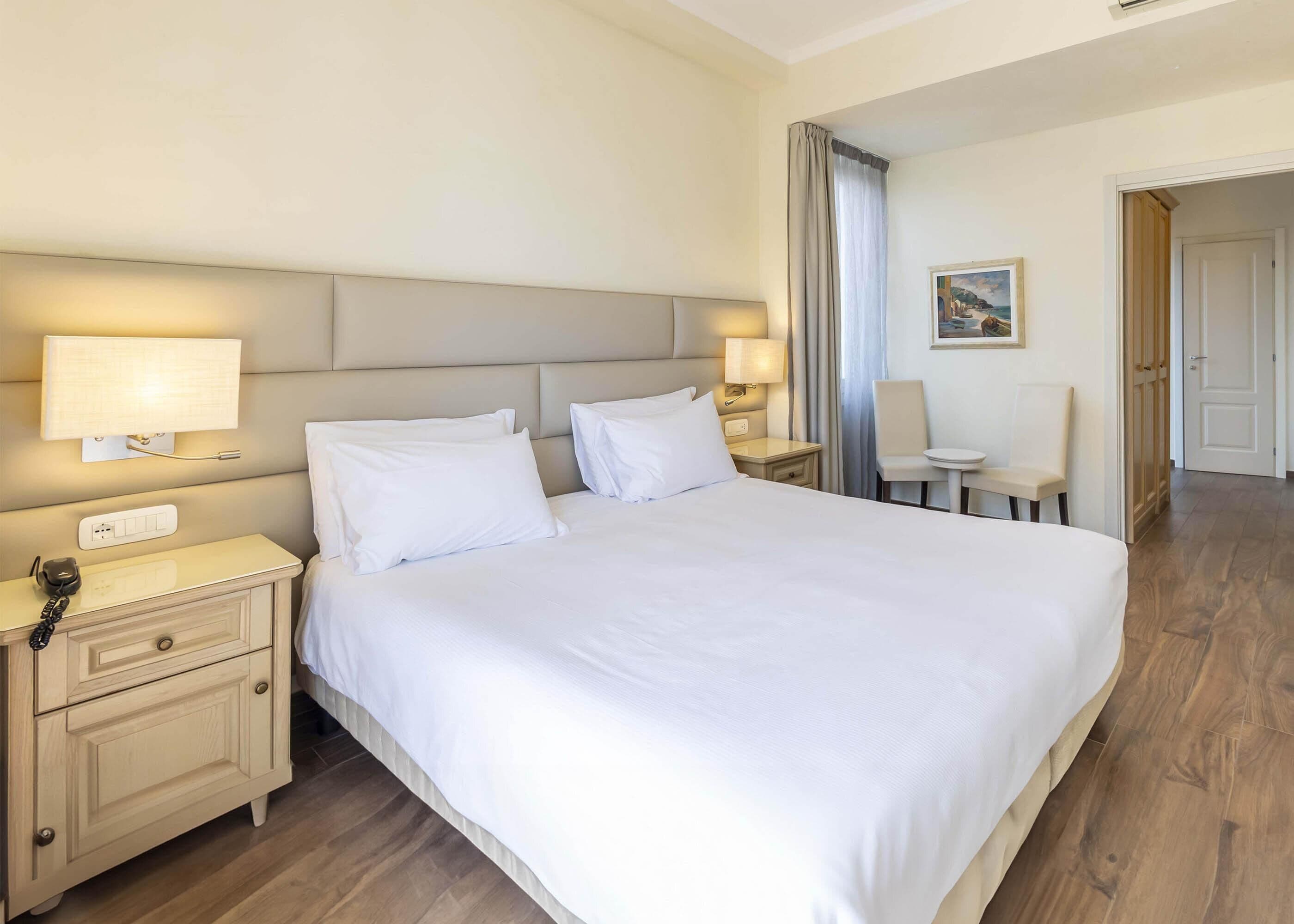 A hotel room with a large bed, bedside tables with lamps, a telephone, and a chair.