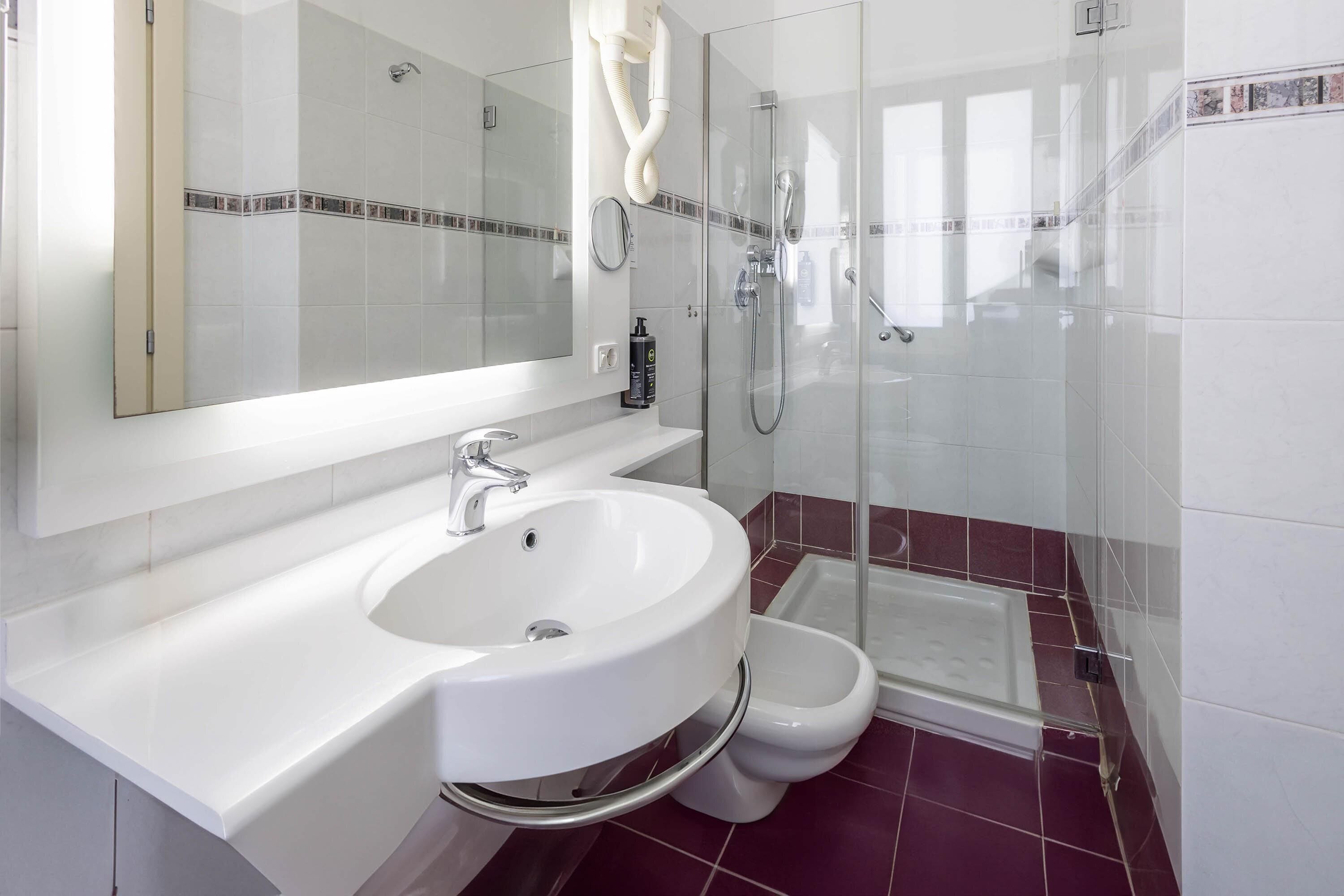 A modern bathroom with a white sink, a mirror, a shower, and a toilet.