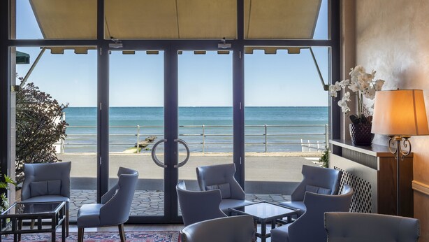 A beachside room with large windows, a view of the ocean, and a seating area with chairs and tables. - B&B Hotel Diano Marina Palace (Diano Marina)