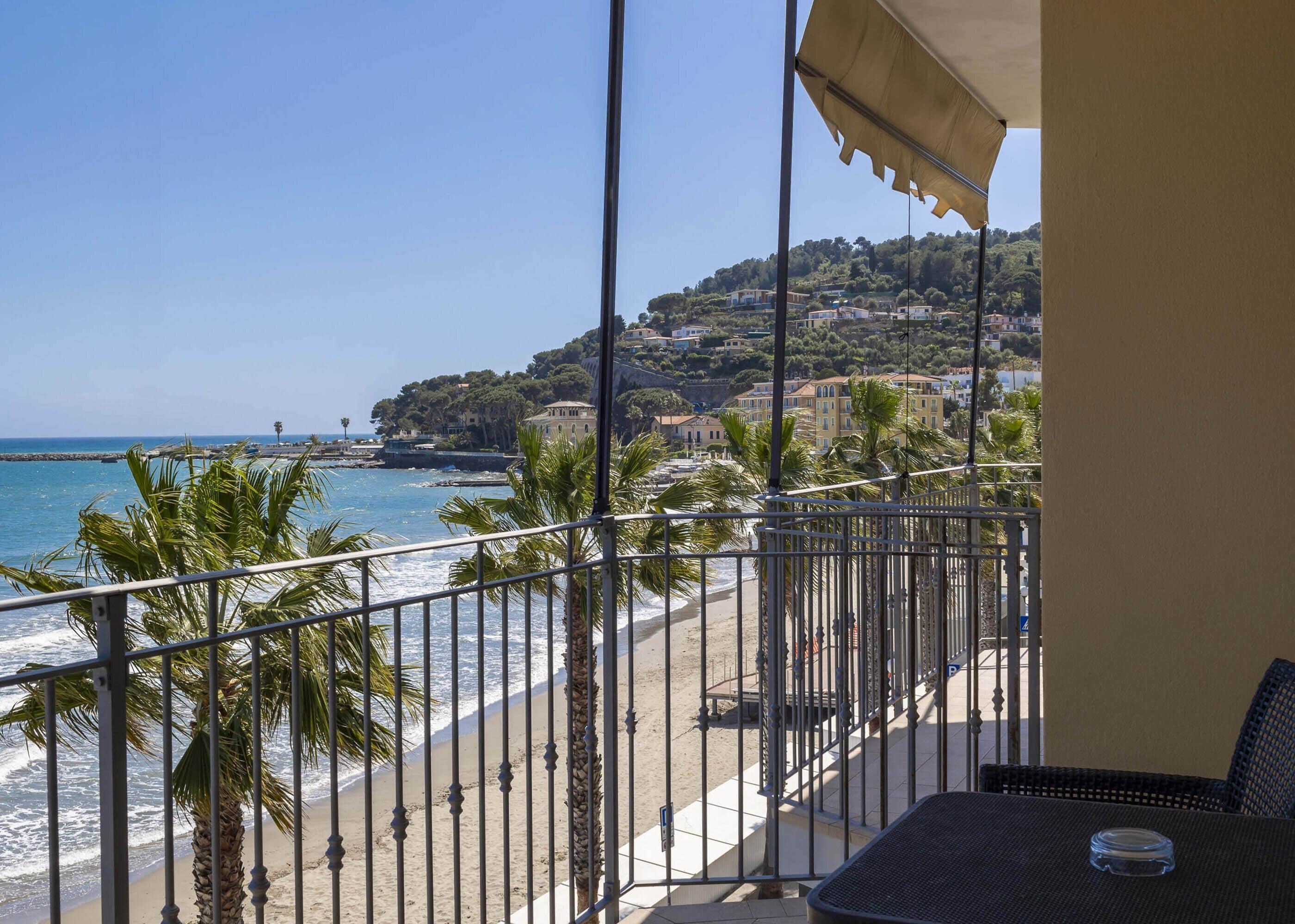A balcony with a view of the beach and a hillside with buildings.