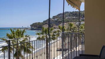 A balcony with a view of the beach and a hillside with buildings.