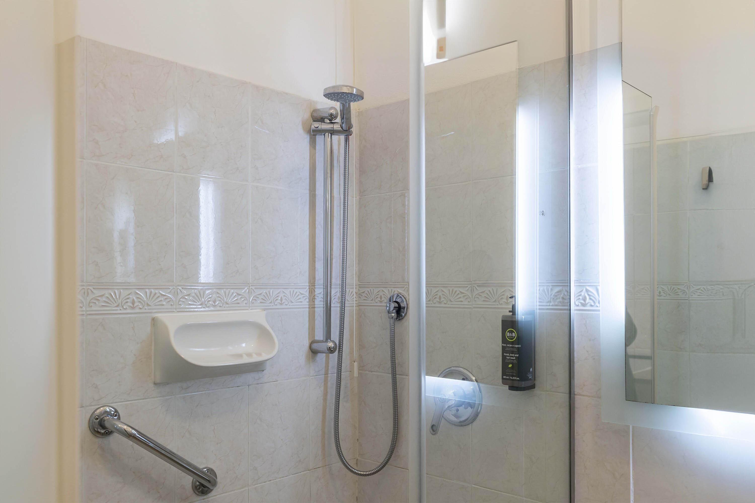 A glass-enclosed shower area with a handheld showerhead, a handheld shower attachment, and a handheld shower control.