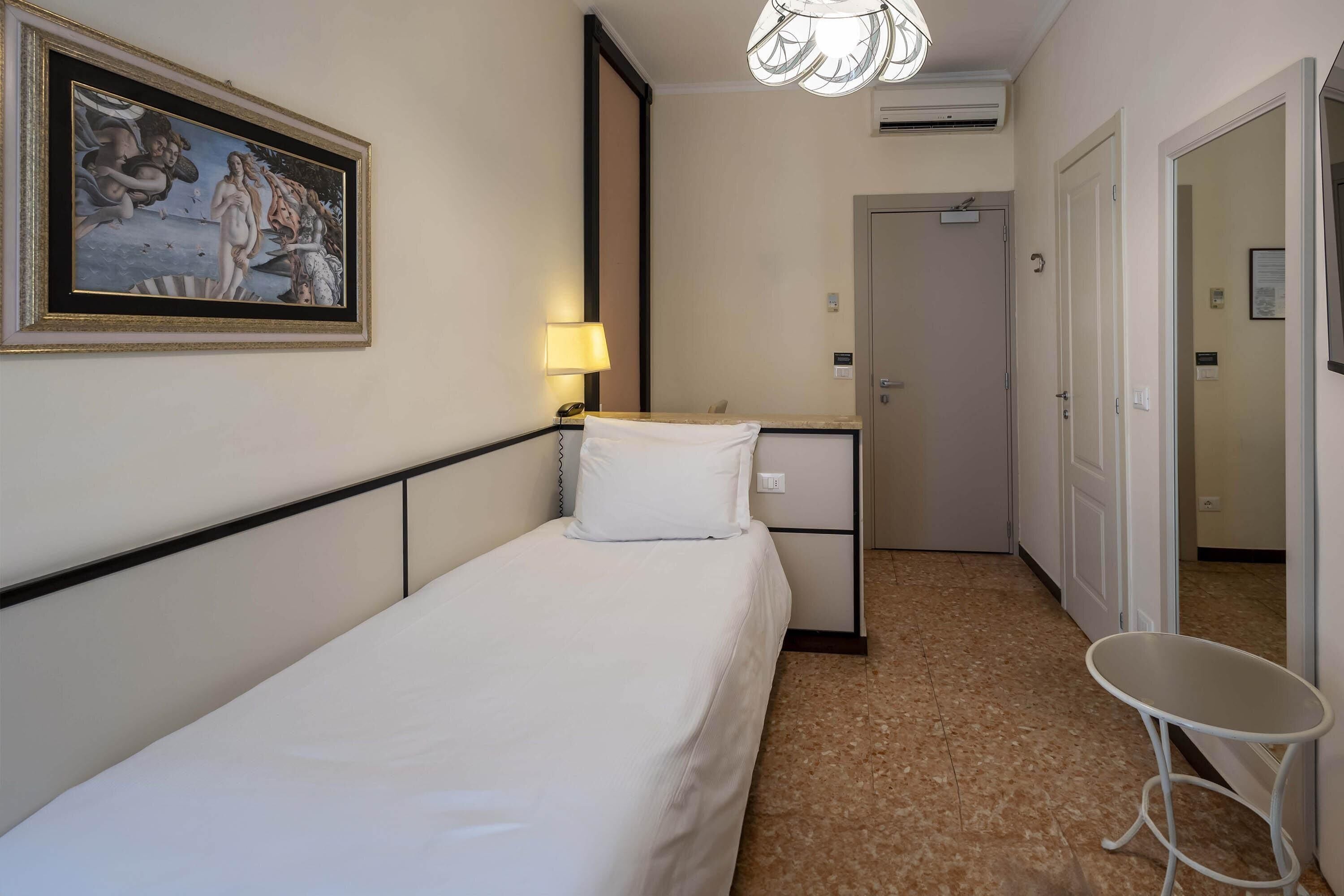Una habitación de hotel con cama, mesita de noche, lámpara y un cuadro en la pared.