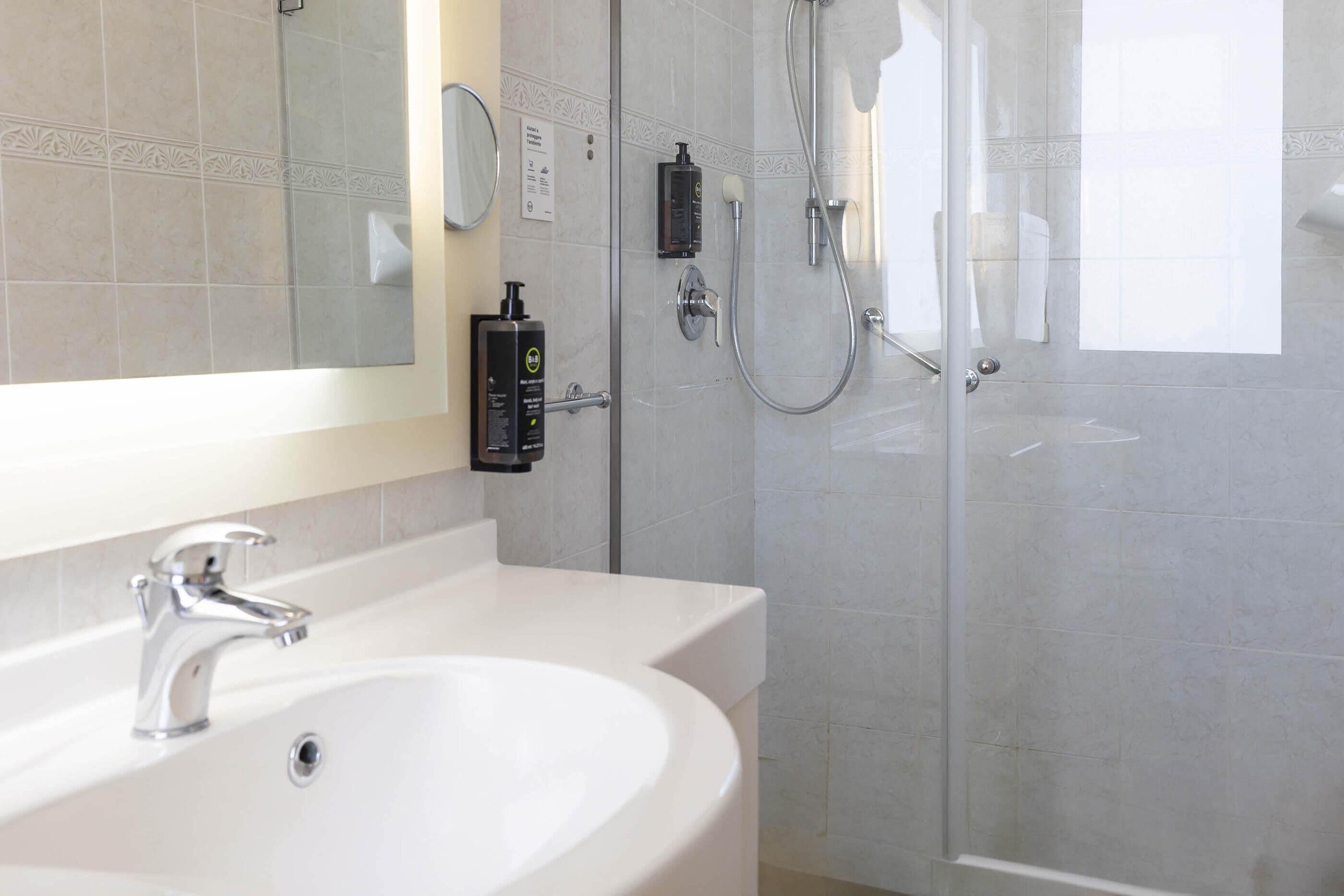 Ein modernes Badezimmer mit einem weißen Waschbecken, einem Spiegel, einer Duschkabine aus Glas und einer Handbrause.