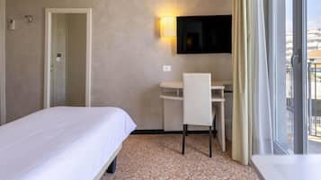 A hotel room with a bed, a desk, a chair, a TV mounted on the wall, and a window with curtains.