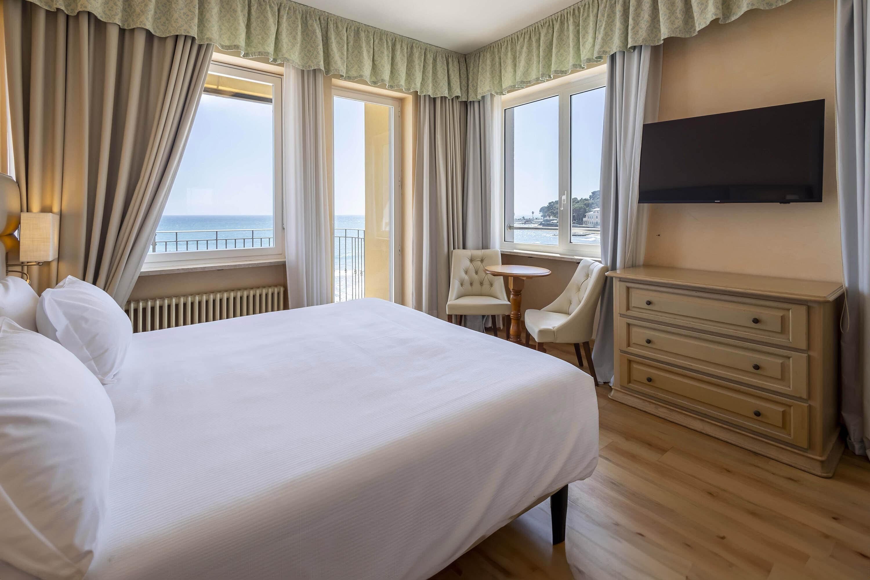 Camera d'albergo con un letto grande, una scrivania, una sedia, una televisione e vista sul mare.