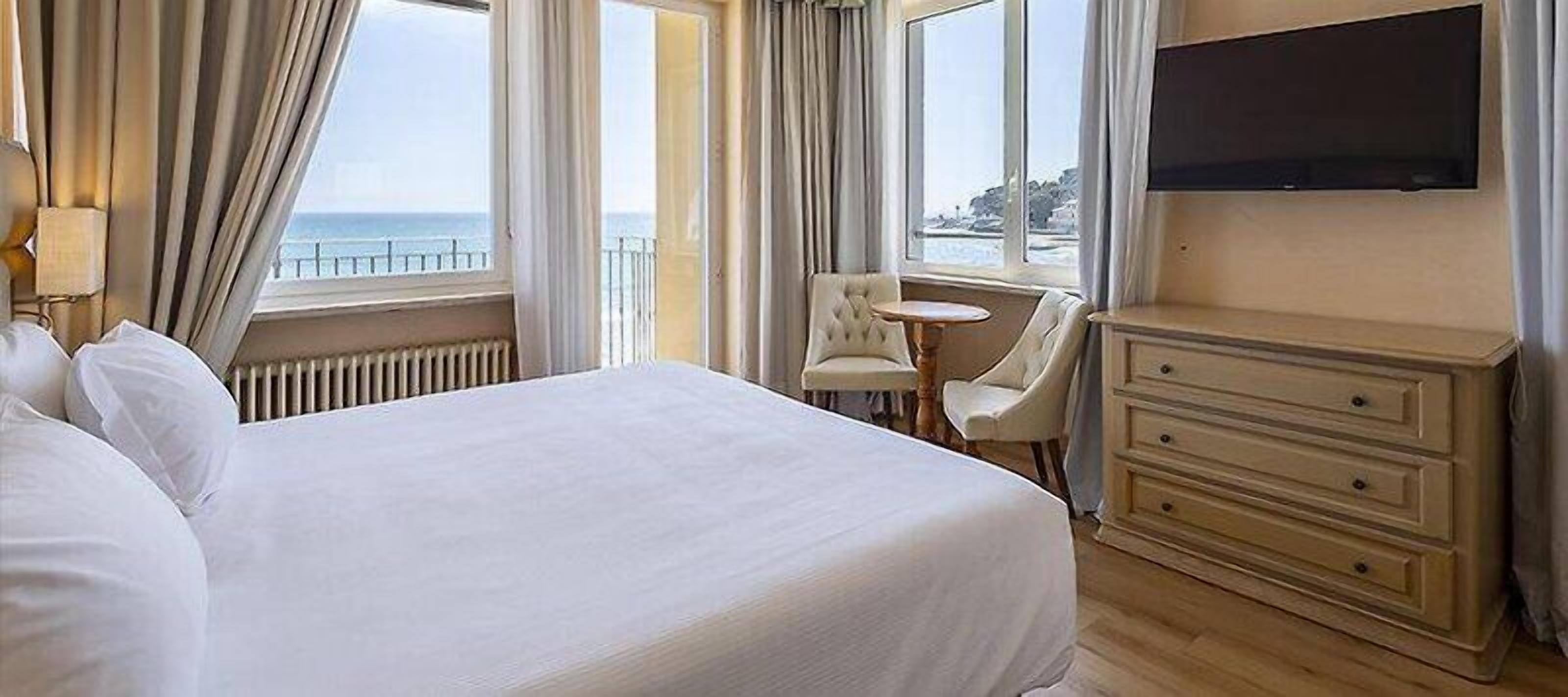 Ein Hotelzimmer mit einem großen Bett, einem kleinen runden Tisch, einem Stuhl, einem Schminktisch und einem Fernseher.