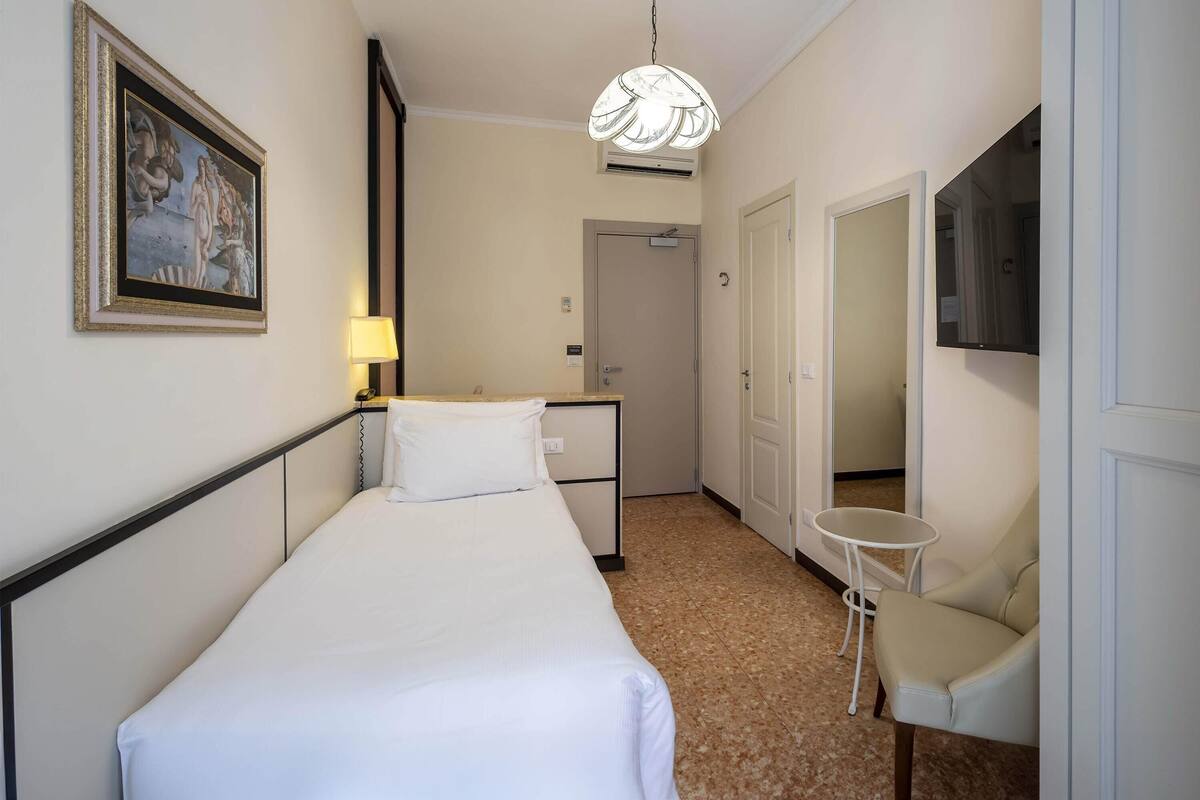 Ein Hotelzimmer mit Bett, Schreibtisch, Stuhl, Lampe, einem Bild an der Wand und einem Fernseher.