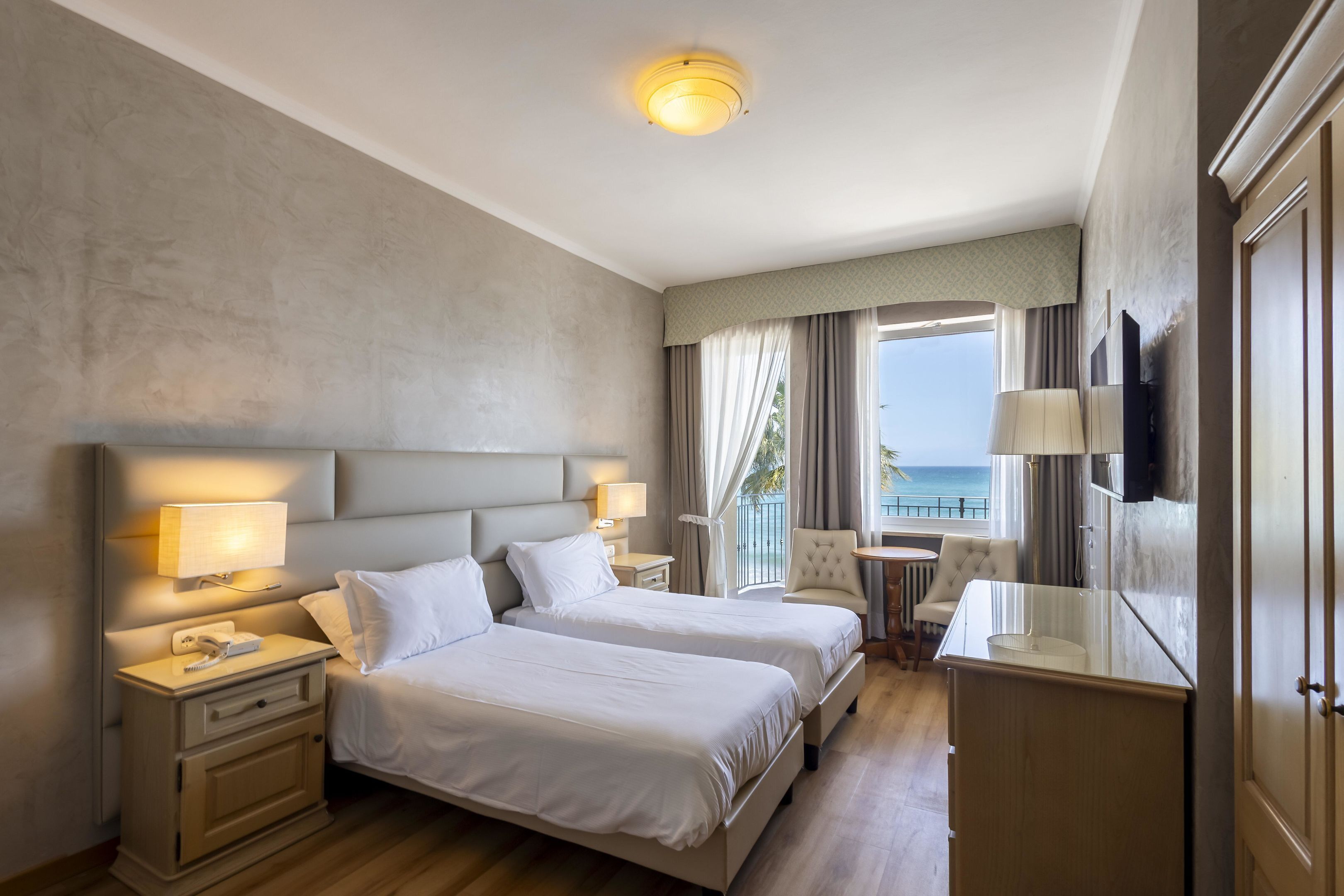 Habitación de hotel con dos camas, un escritorio, una silla, televisión y vista al océano.