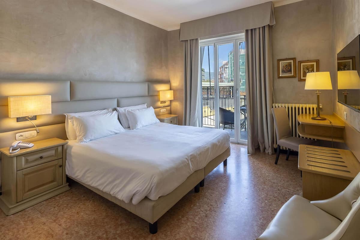 Ein Hotelzimmer mit einem großen Bett, Nachttischlampen, einem Schreibtisch mit Stuhl und Blick auf den Balkon.