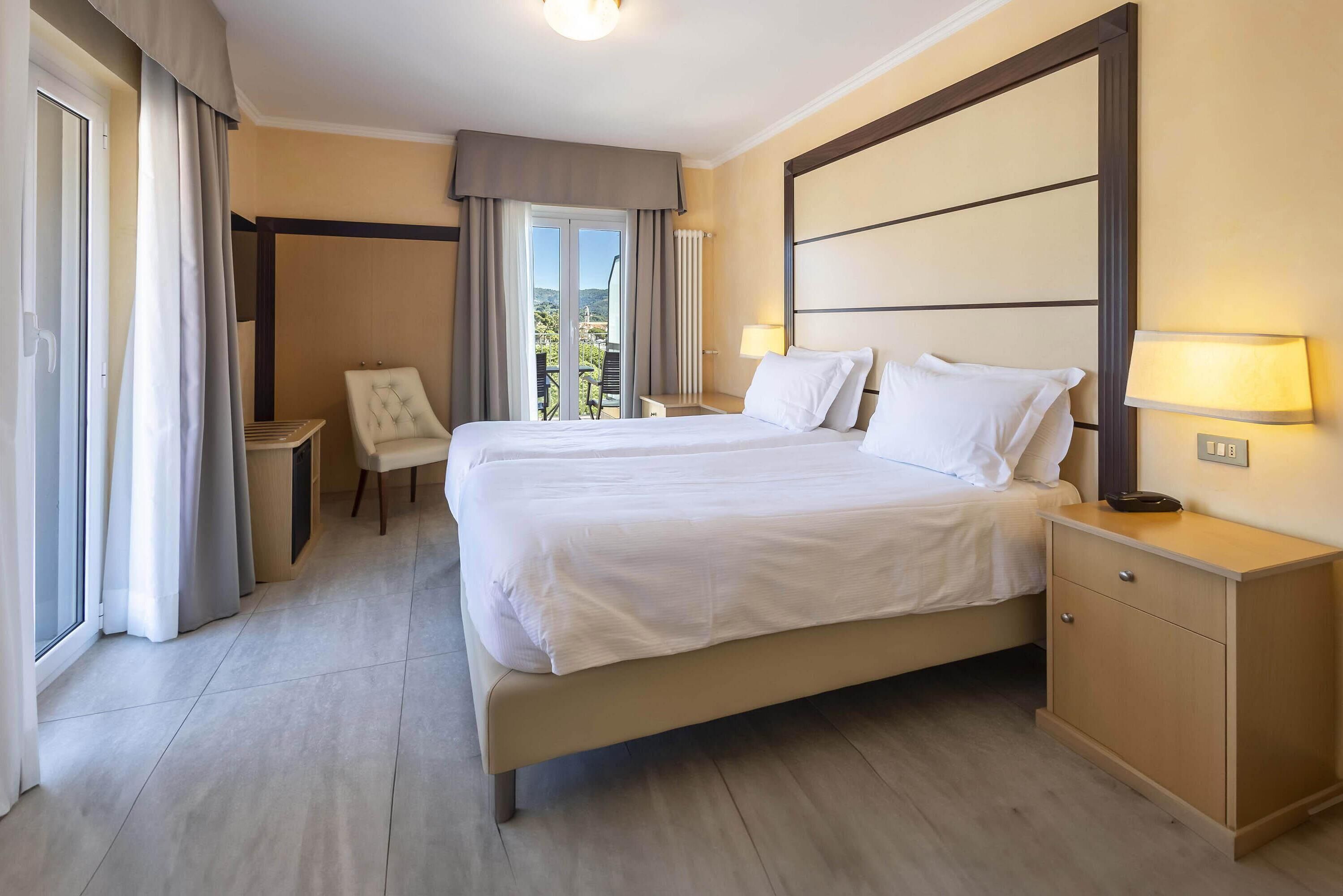 A hotel room with a large bed, bedside tables, a chair, and a view of the outdoors.