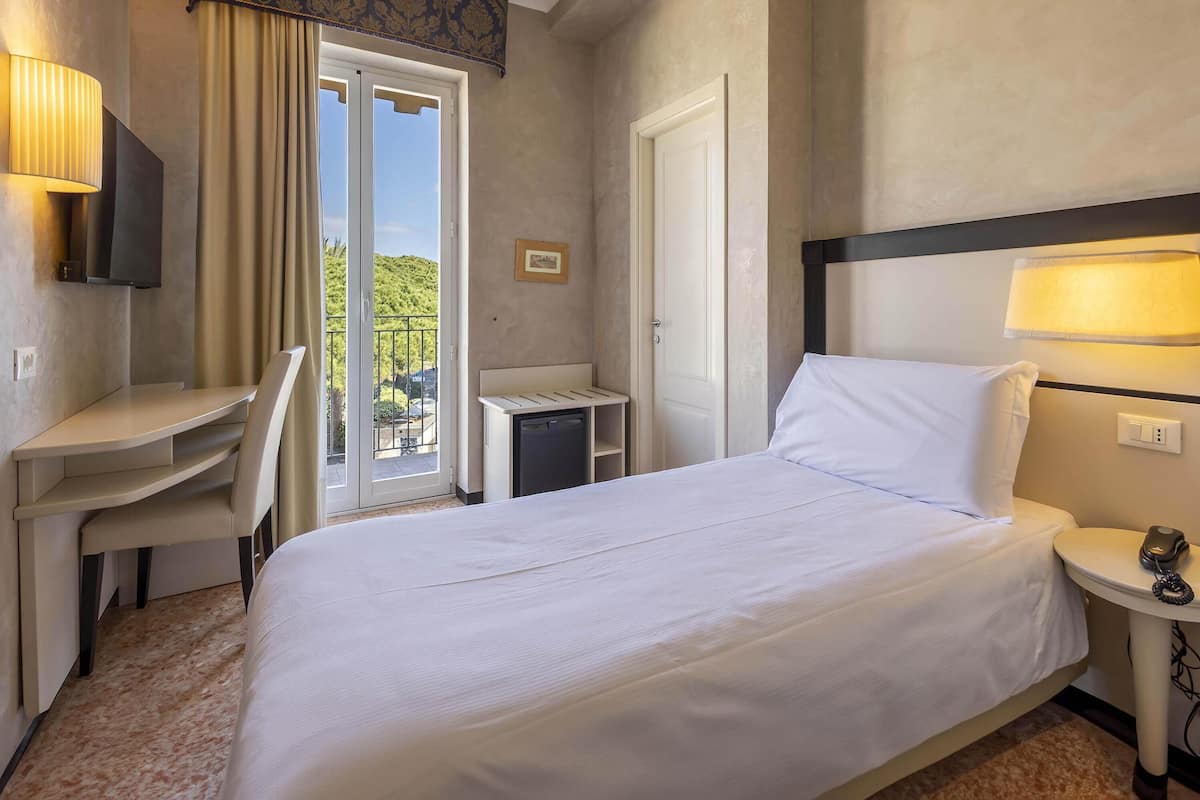 Ein Hotelzimmer mit einem Bett, einem Schreibtisch, einem Stuhl, einem kleinen Tisch, einer Lampe und einem Fernseher.