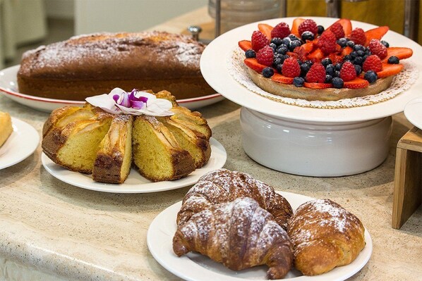 A variety of baked goods including a cake, a fruit-topped tart, a bundt cake, and croissants on a marble countertop.