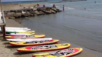 Várias pranchas de bodyboard coloridas alinhadas na areia, perto da água.