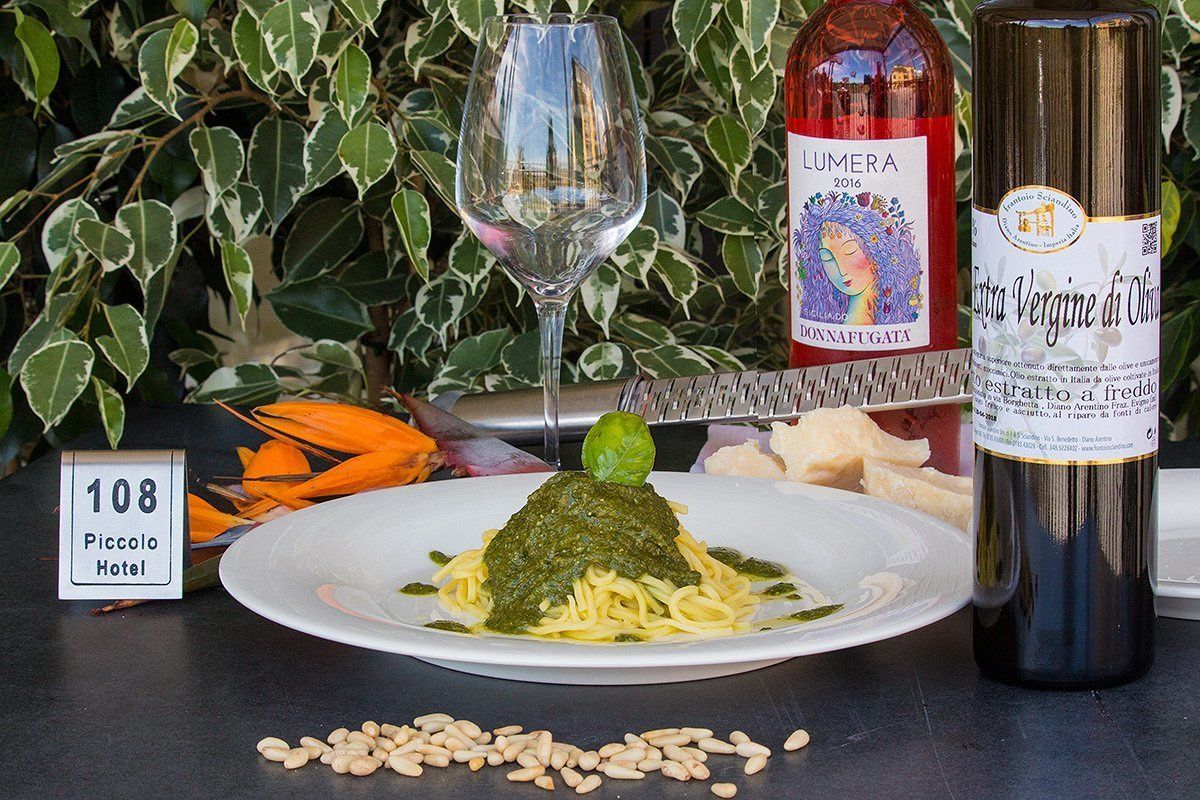 Un plato de pasta con salsa verde, una botella de vino y una copa de vino sobre una mesa con una señal que indica la habitación 108 en el Hotel Piccolo.